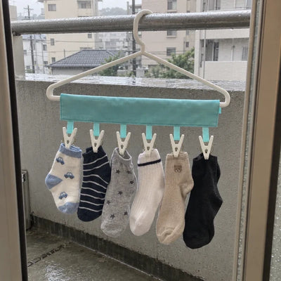 雨の日のベランダで、小さな靴下を物干しに干している写真。
